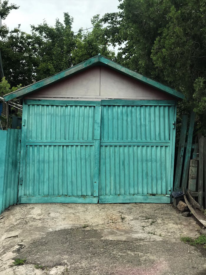 gallery-1 Rustic turquoise wooden garage door against a natural backdrop, offering a vintage charm.