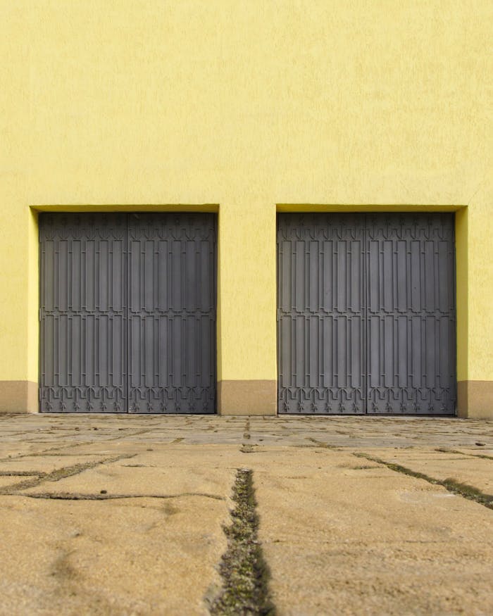 gallery-4 Yellow wall with two closed grey garage doors creates a minimalist urban scene. Ideal for architecture and design concepts.