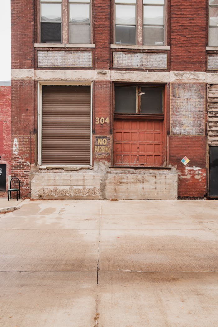 about-img A vintage red brick warehouse facade with large doors and a no parking sign.