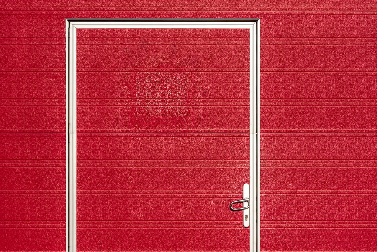 services-01 Minimalist image of a bold red garage door with a white frame and textured surface.