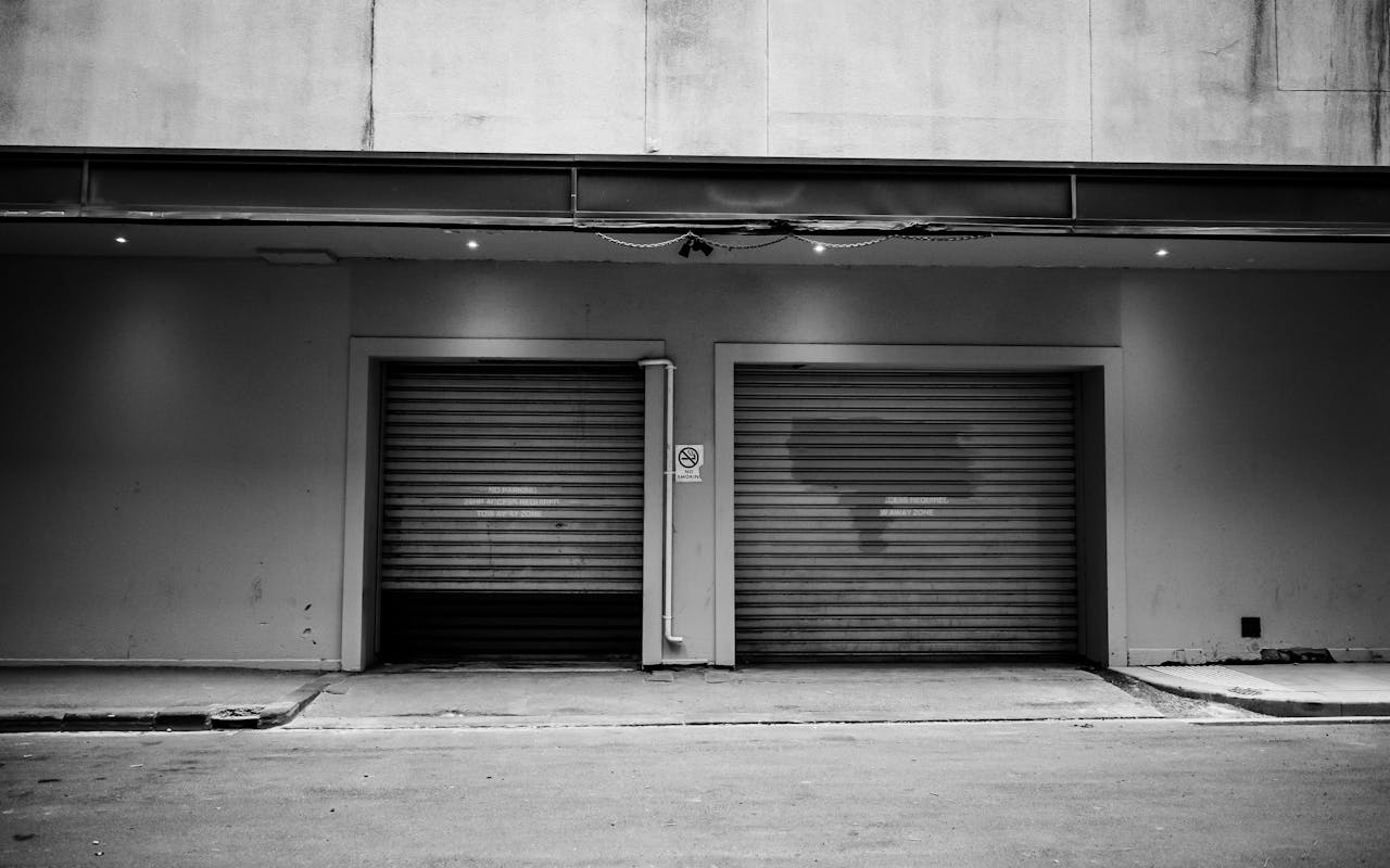 services-03 A monochrome urban exterior with two closed garage doors and a concrete wall.